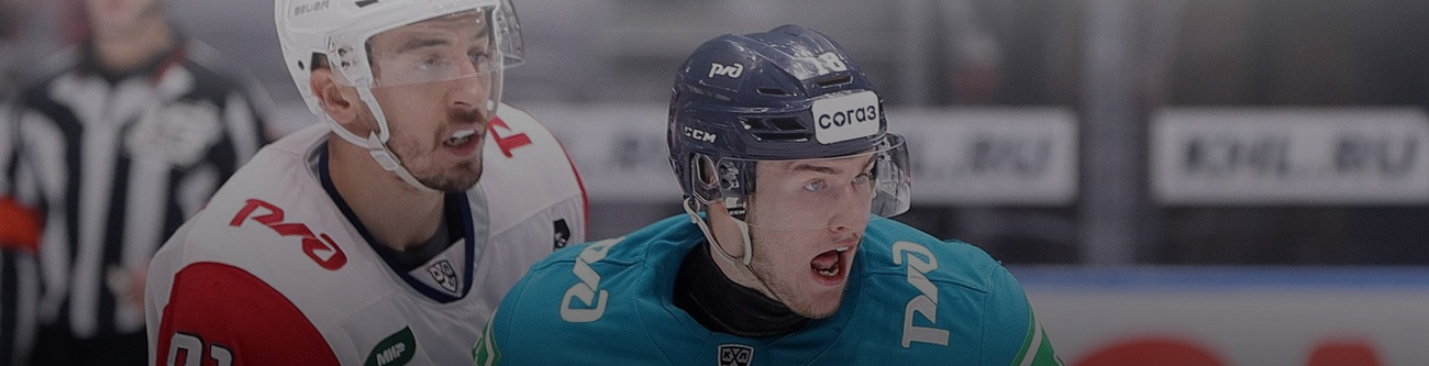 На изображении два хоккеиста в защитных шлемах на льду. Один в форме с красным и белым цветами, другой — в бирюзовой. На фоне размыт судья. Видна часть борта с надписью KHL.RU